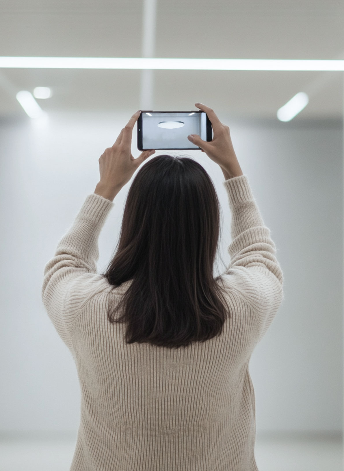 A lady holding up her smartphone at a large atrium ceiling with Hacel's Lumera pendant hanging down in augmented reality.